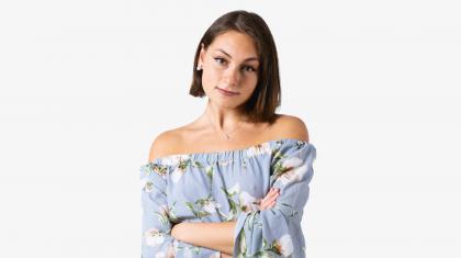 A headshot of a woman looking forward with dark brown hair and a light blue flowery top