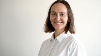 Woman smiling at the camera, she's wearing a white shirt and has medium dark hair.