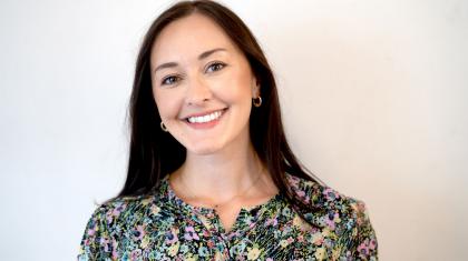 Woman with long dark hair, wearing a flower patterned top smiles at the camera