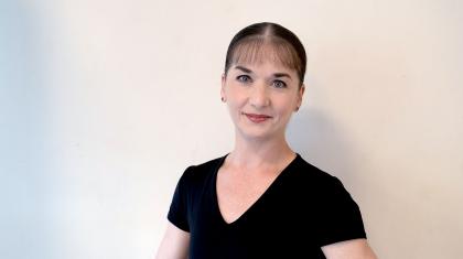 Woman with dark hair tied back, wearing a black top, smiles enigmatically at the camera