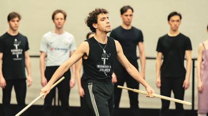 Dancer strides confidently across the stage with a weapon in each hand, is arms slightly spread threateningly
