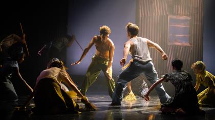 Two dancers, one bear chested in green trousers, the other in blue trousers with a white vest, fighting