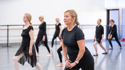 A cohort of participants on the Over 55s class standing one foot in front of the other, arms by their side or on the leading thigh