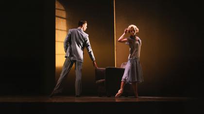 Dancers on stage in 1920 clothing, her a blue flapper dress, him is a sharp grey suit