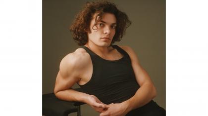 Man in black vest with medium length, curly hair looking intently at the camera