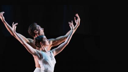 Two dancers in white looking into the distance, hands raised