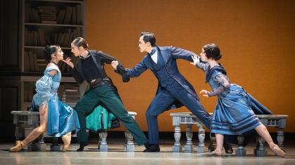 A woman in a blue dress looks lovingly at a woman holding her chin, she is held from behind by a man looking angry and be him is another woman looking concerned