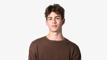 A headshot of a man with dark hair in a brown jumper stood facing the camera