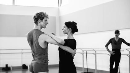 Two dancer in the rehearsal room practicing a tango, bodies apart, one hand holding the partner's, her other hand resting on his shoulder, his on her back, each looking intently at the other